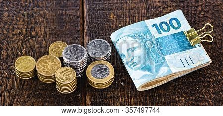 Money And Banknotes Of 100 Reais From Brazil, Coins From One Real On A Well Lit Rustic Wooden Backgr