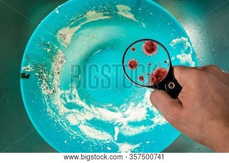 A Hand With A Magnifying Glass Is Aimed At Dirty Dishes, Bacteria Are Visible In The Magnifying Glas