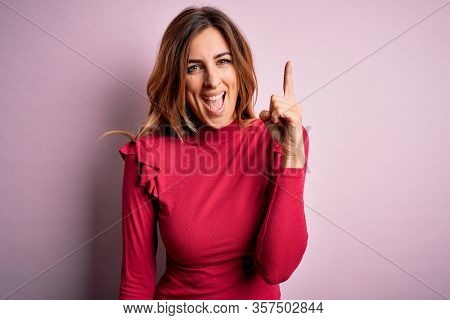 Young beautiful brunette woman wearing casual sweater stnding over pink background pointing finger up with successful idea. Exited and happy. Number one.