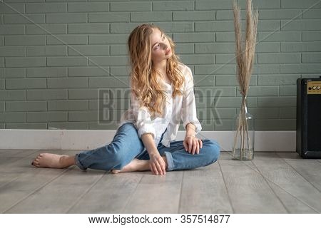 Young Beautiful Woman With Bare Feet Sitting On The Floor Next To Subwoofer And Glass Vase With Dry 