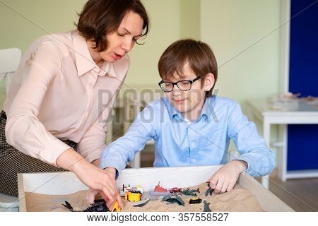 The Boy With The Teacher With Glasses Is Sand Therapy On The Table With Light.