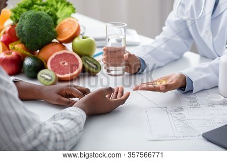 Cropped Of African American Woman Dietologist Giving Pills And Glass Of Water To Female Patient, Foo