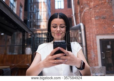 Stylish Hipster Girl With Dark Hair Wearing In Trendy Spectacles Online Banking Via Mobile Phone Whi