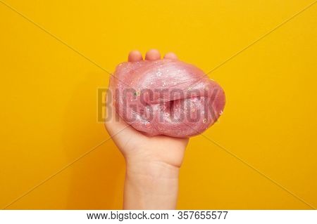 Pink Slime With Sequins, In A Childs Hand, On A Yellow Background. Creativity, Creativity And Experi