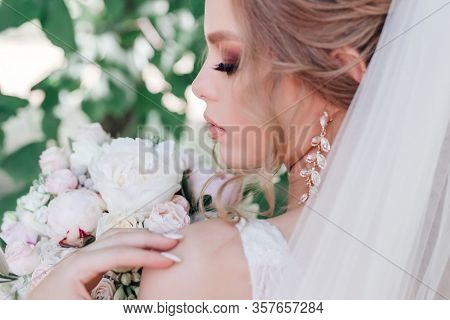 Close-up Of Beautiful Bride With Wedding Flowers Bouque In Park. Bride With Wedding Makeup And Hairs