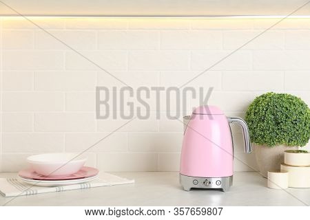Modern Electric Kettle, Dishes And Houseplant On Counter In Kitchen