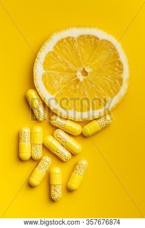 Vitamin capsules. Vitamin C pills and slice of lemon on yellow background. Top view.