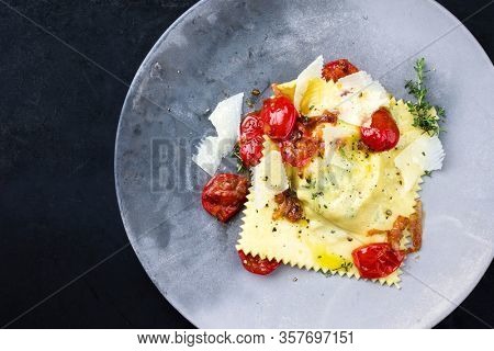 Traditional Italian ravioli pasta offered with parmesan cheese and fried tomatoes as top view on a modern design plate with copy space left