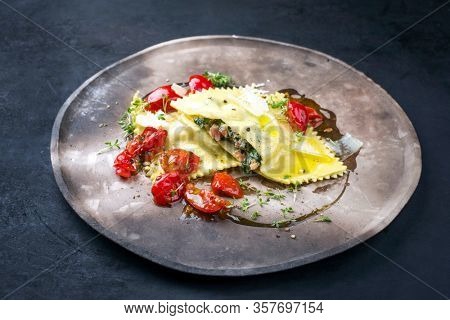 Traditional Italian ravioli pasta offered with salmon spinach filling and fried tomatoes as closeup on a modern design plate 
