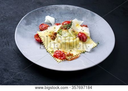 Traditional Italien ravioli pasta offered with parmesan cheese and fried tomatoes as closeup on a modern design plate 