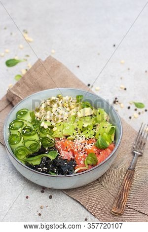 Salted Salmon Poke Bowl With Avocado, Sea Cale, Cucumber, Sesame Seeds And Bean Sprouts On Grey Back