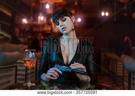Sexy Young Woman Sits At A Table And Holds A Gun In Her Hands.