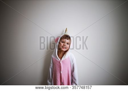Portrait Of Little Todder Girl Standing Next To A White Wall Wearing Unicorn Kigurumi And Looking At