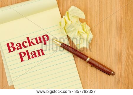 Backup Plan Message On A Yellow Legal Notepad Paper With Crumpled Paper And Pen On Wood Desk