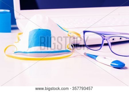 Protective Mask Thermometer And Glasses On Medical Desk With White Laptop Background - Concept Of Co