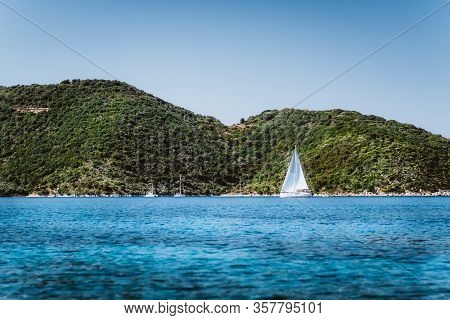 Greece Ithaki Island, White Sail Yacht In Open Blue Sea With Green Island In Background