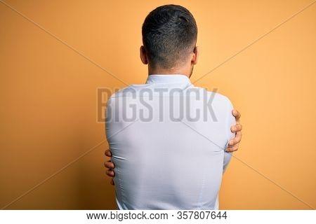 Young handsome businessman wearing tie and glasses standing over yellow background Hugging oneself happy and positive from backwards. Self love and self care