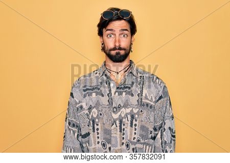 Young handsome hispanic bohemian man wearing hippie style and sunglasses puffing cheeks with funny face. Mouth inflated with air, crazy expression.