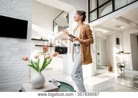 Woman Having Some Business Work, Standing With A Smart Phone In The Modern Living Room At Cozy Home.