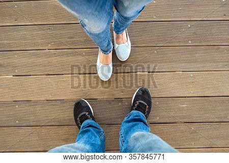 Top Down View Of Legs In Denim Jeans Pants And Light Summer Sneakers Standing On Wooden Floow.