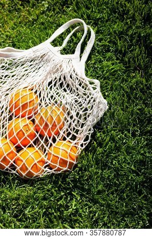 White Cotton Eco String Bag With Oranges On A Grass. Good Idea For A Picnic. Zero And Eco Waste. No 
