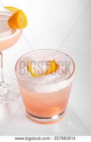 Negroni sour cocktail close up. Alcohol strong aperitif drink in glasses side view. Beverage with vermouth, liqueur, gin, orange and egg white in drinkware. Cocktail portions in glassware