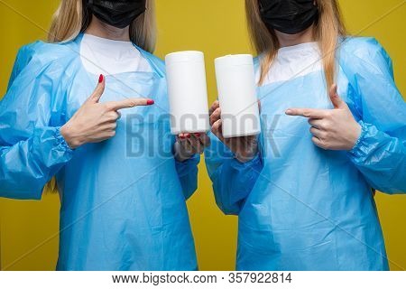 Young Beautiful Girls In A Disposable Medical Gowns And With A Masks On Their Faces Holds Wet Antiba