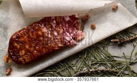 Dried Sausage Made Of Beaver Meat. Cut With Slices On Parchment With Pine Buds Closeup. Flooring Mad