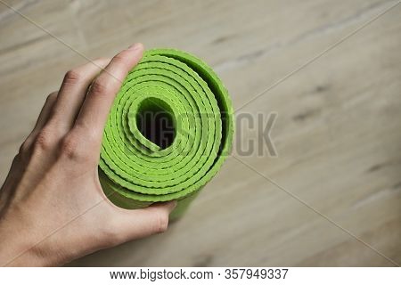 A Woman's Hand Holds A Standing Yoga Mat In Green. Healthy Lifestyle. Light Background, Blur Of The 