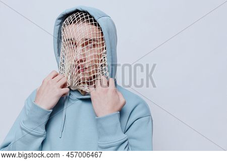 Tortured, Suffering From Problems, A Man With A Mesh On His Face Stands In A Light Blue Hoodie On A 