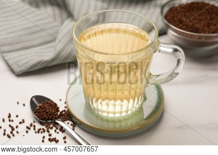 Glass Cup Of Buckwheat Tea And Granules On White Marble Table
