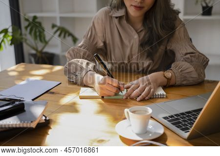 Young Woman Using Computer Laptop And Making Noes On Notebook.