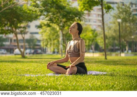 A Woman In Brown Sport Bra And Black Short Sitting On Yoga Mat Doing Maditation With Hand Together A