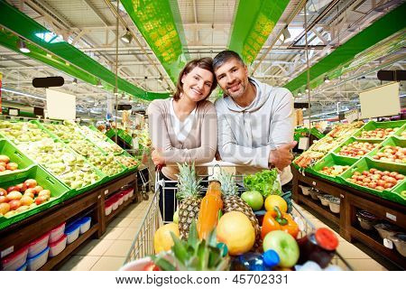 Bild von glückliches Paar mit Einkaufswagen voller Produkte, Blick in die Kamera im Supermarkt