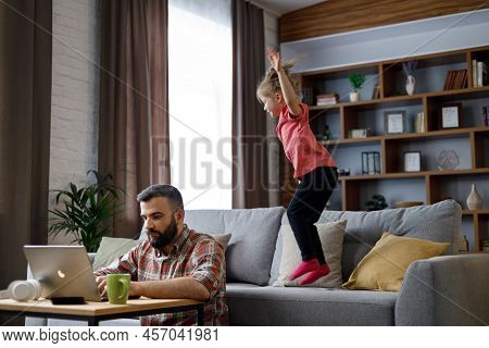 Young Handsome Man Work From Home At Laptop, Focus Attention On Laptop Screen While His Little Daugh