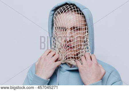 Tortured, Suffering From Problems, A Man With A Mesh On His Face Stands In A Light Blue Hoodie On A 