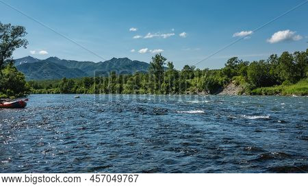 Ripples And Foam Are Visible On The Surface Of The Mountain River. An Inflatable Rafting Boat Is Moo