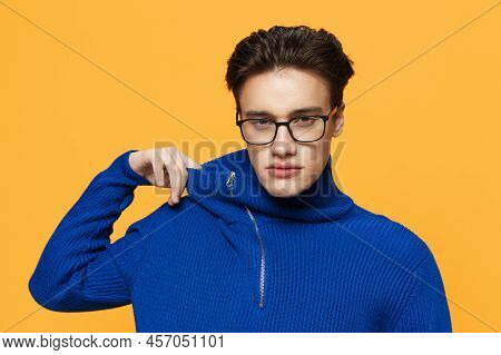 An Attractive Young Man Stands On An Orange Background In A Blue Zip-up Jacket And Black Eyeglasses 