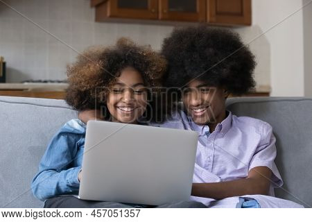 Cheerful Teenage African Couple Sit On Sofa With Laptop