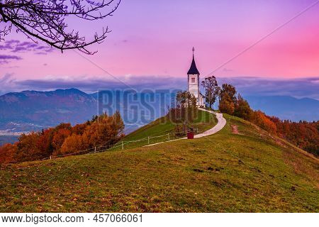 Beautiful Sunset Landscape Of Church Jamnik In Slovenia On Green Hill With The Trees And Pink Sky