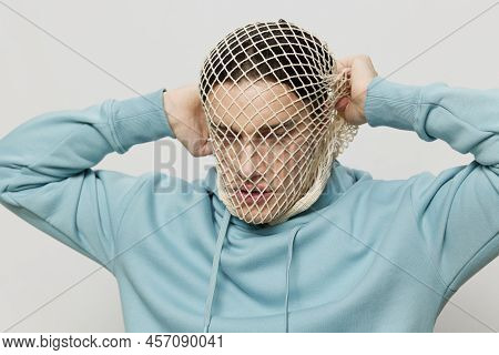 Tortured, Suffering From Problems, A Man With A Mesh On His Face Stands In A Light Blue Hoodie On A 