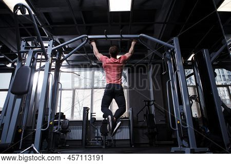 Rear View Fulllength Shot Of An Athletic Muscular Man Doing Pull-ups In Crossover Gym Machine