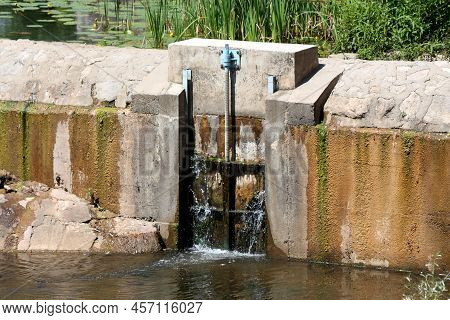Closed Old Leaking Partially Rusted Metal River Dam Gates Covered With Moss Built Between Thick Conc