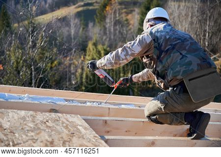 Male Builder Doing Thermal Insulation On Roof Of Wooden Frame House. Man Worker Spraying Polyurethan