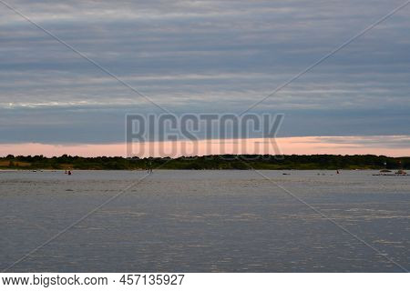 Dusk In Blue And Pink Hues With Calm Waters And Land Strip.