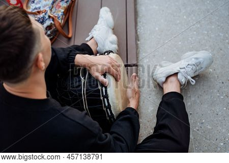 Hipster Sits On The Floor Playing A Drum, A Guy Street Musician Beats His Palm On The Djemba, Africa