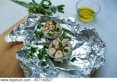 Two garlic heads on foil with oil and herbs. Preparation of garlic for baking. Preparation of garlic
