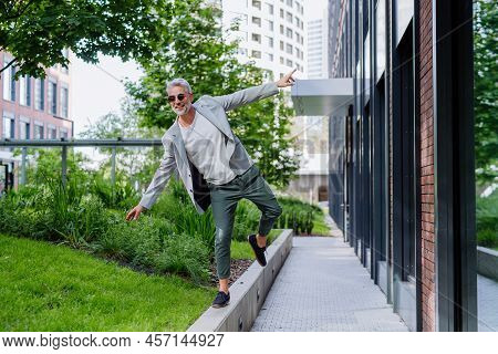 Fun Portrait Of Happy Energetic Mature Businessman With Arms Outstretched Balancing On Wall , Feelin