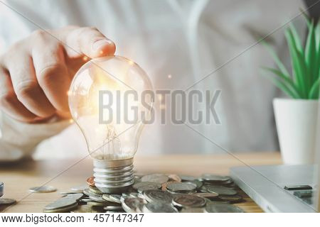 Businessman Holding Lightbulb On Coins Stacking On Desk With Note For Planning Money Finance.saving 