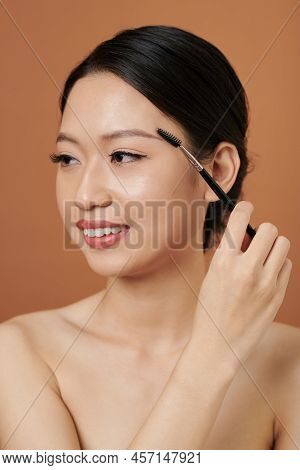 Studio Portrait Of Smiling Vietnamese Young Woman Brushing Her Eyebrows